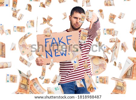 Young handsome man holding fake news message banner with angry face, negative sign showing dislike with thumbs down, rejection concept
