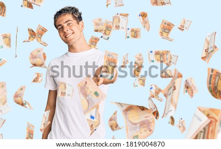 Young handsome man wearing casual white tshirt smiling cheerful offering palm hand giving assistance and acceptance.