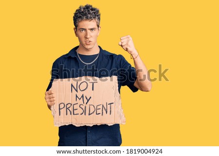 Young handsome man holding not my president protest banner annoyed and frustrated shouting with anger, yelling crazy with anger and hand raised 