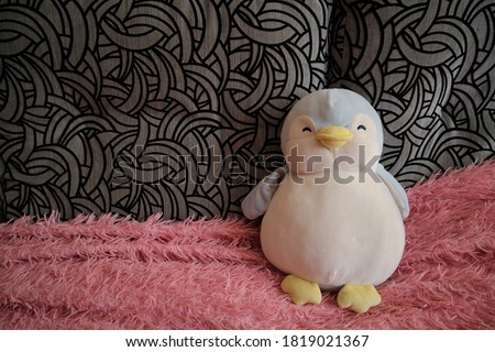 Cute penguin toy on sofa at home. Space for text