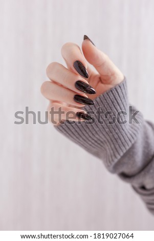 Female hand with long nails and gray black manicure with bottles of nail polish