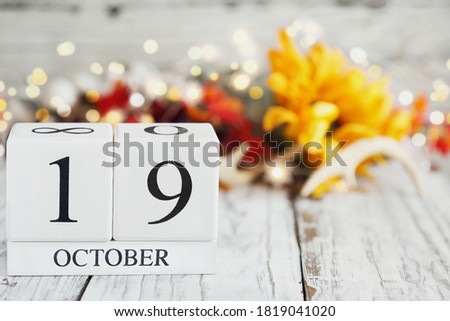 White wood calendar blocks with the date October 19th and autumn decorations over a wooden table. Selective focus with blurred background. 