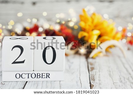 White wood calendar blocks with the date October 20th and autumn decorations over a wooden table. Selective focus with blurred background. 