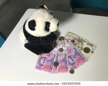 Toy Panda waiting on coins made of 100 and 200 500 Ukrainian coins composition on white table Great composition Macro shooting conceptual Ukrainian money shoot buying now.