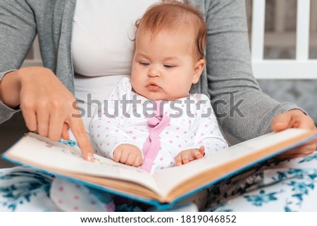 A mother holds the child in her arms and points to the picture in the book. Portrait of a baby and books close-up. The concept of motherhood and childhood