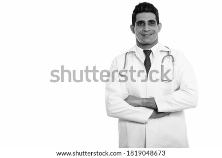 Studio shot of young happy Persian man doctor smiling with arms crossed