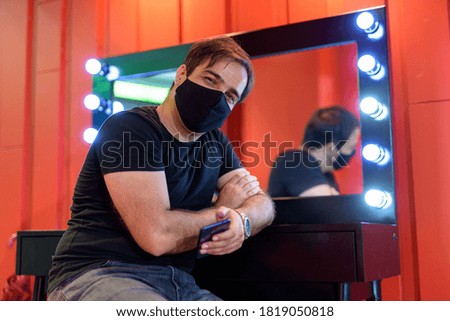 Persian man with mask sitting and leaning against mirror in the makeup room