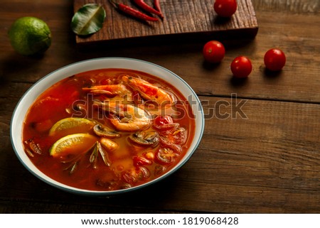 Tom yam soup with shrimp and lime in a light bowl next to lime, pepper chili and cherry.