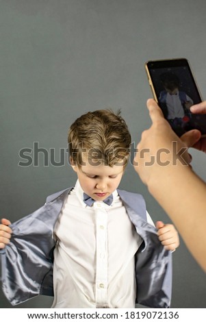 Mom takes pictures of her son on the phone. Gray background.