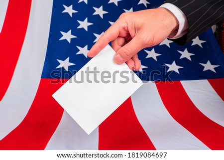 US President Election. An American is voting in the 2020 election. A man's hand with a ballot on the background of the American flag. A person at a polling station in the United States.