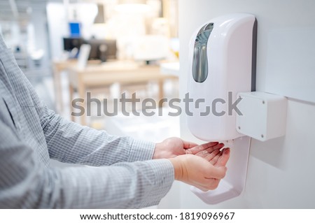 Male hands using automatic alcohol dispenser for cleaning hand in office. Infection prevention concept. Save and clean in public building. Royalty-Free Stock Photo #1819096967