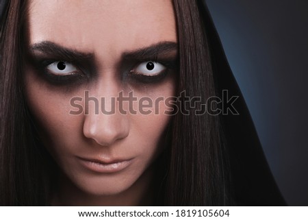 Mysterious witch with spooky eyes on color background, closeup