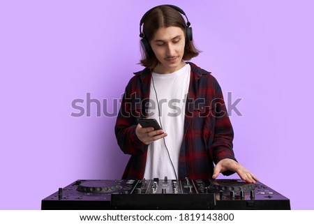 modern club DJ playing mixing music on vinyl turntable, isolated in studio. caucsaian male perform techno style music, enjoy playing on equipment, use smartphone