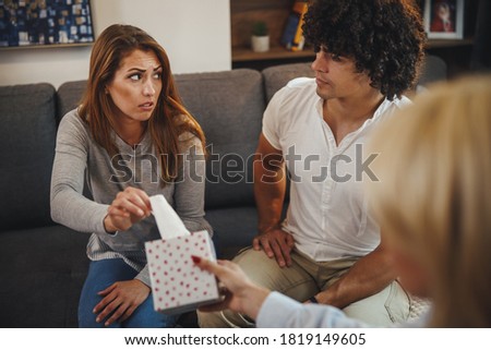 Shot of a female psychotherapist offering tissues to her young couple patients during a counseling session on a sofa inside of a living room.