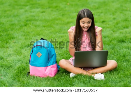 happy girl sitting on green grass with laptop. Start up. child playing computer game. back to school. education online. knowledge day. kid learning private lesson. blogging.