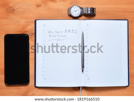 top view of a notebook with a pen smartphone and a clock, new goals in the coming year. wooden background, copy space,