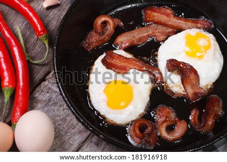 fried eggs with bacon in a frying pan and chili pepper, garlic on the table. top view  Royalty-Free Stock Photo #181916918