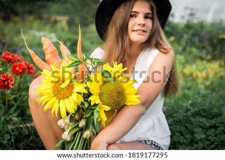 A cute girl is sitting on the grass in the village. bouquet of vegetables. yellow sunflower, pepper, pumpkin and garlic. Lifestyle