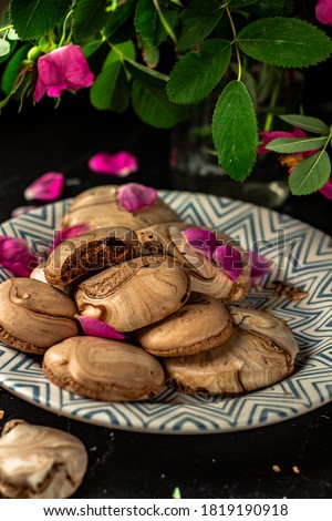 Homemade Marble Chocolate Meringue cookies with cocoa powder on a dark background with pink dogrose flowers. Close-up. Low Key. Vertical Orientation.