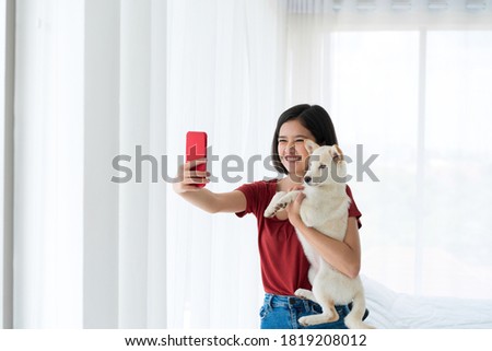 A woman with a white dog taking a picture with a mobile phone