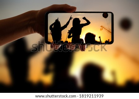 Silhouette of hand using camera phone to take pictures and videos at pop concert, festival.