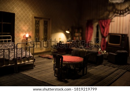 A realistic dollhouse living room with furniture and window at night. Artwork table decoration with handmade realistic dollhouse. Man wathing retro style Television in dark room. Selective focus.