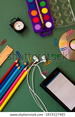 Colorful school supplies on greenboard with copy space,mini vintage alarm clock and smart phone with blank white screen.