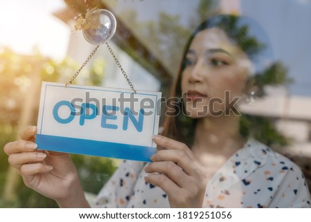 young woman owner turning open sign in door of store