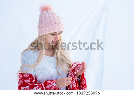 Portrait of a cute woman against the snow in a pink hat and red plaid posing for the camera.