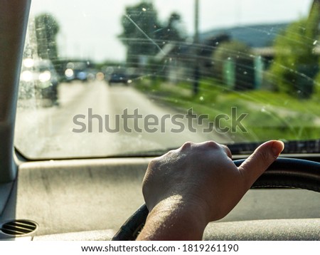 tired woman's hand without a manicure is on steering wheel, car with dirty glass is driving in suburbs, selective focus