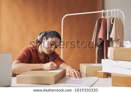 Young girl working at the table she accepting and completing orders signing the address on them