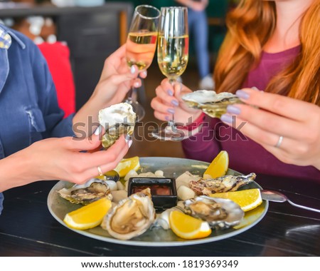 Fresh oysters as well as fine dining, two young attractive woman eating oysters in restaurant and drinking champagne. Eating out concept, dinner in restaurant. Royalty-Free Stock Photo #1819369349