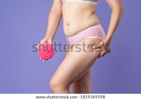 Woman massaging thigh with massage brush on purple background, body care concept