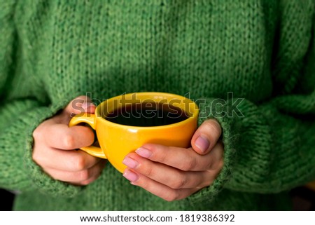 Female hands in a warm green sweater hold a cup of coffee