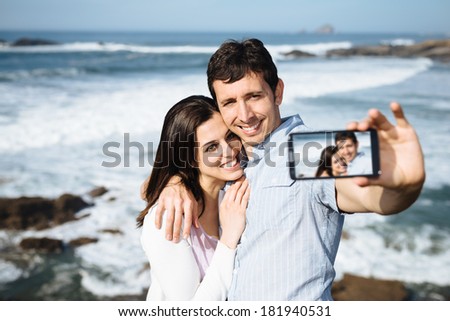 Young couple on honeymoon travel in Asturias coast, Spain, taking selfie portrait photo with smartphone camera.