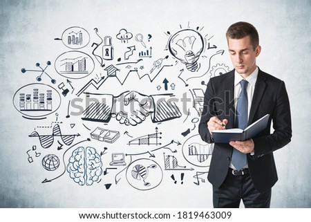 Serious young businessman taking notes near concrete wall with creative business sketch drawn on it. Concept of planning