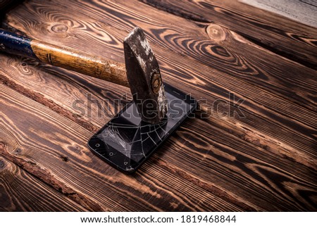 Old big hammer on a broken smartphone display. Studio photo on a wooden background.