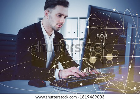 Young businessman using computer in blurry office with double exposure of social media interface. Toned image