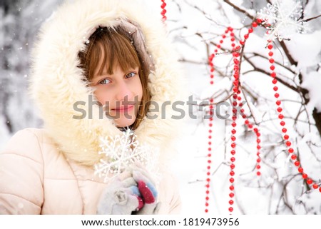 Cute teenage girl portrait in a winter snow-covered Park looking at the camera, smiling and holding a large snowflake. A beautiful winter day in the Park the first snow has fallen and Christmas is com