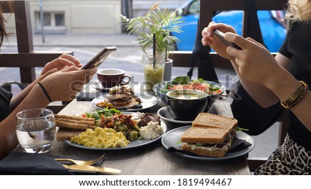 Healthy hipster lunch in the city. Two food blogger friends taking pictures of their food with smartphone.  Royalty-Free Stock Photo #1819494467