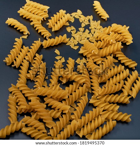 Raw pasta in a spiral shape is sprinkled on a dark dish. Pieces of broken pasta.