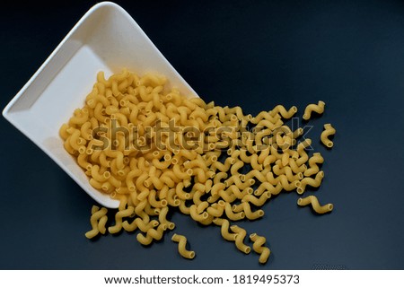 Uncooked spiral pasta sprinkled from a white plate on a dark table.