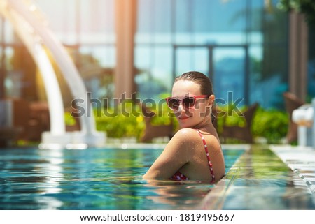 Beautiful young woman in sunglasses smiling in luxury swimming pool during summer holiday. Summer luxury vacation during summer holiday.