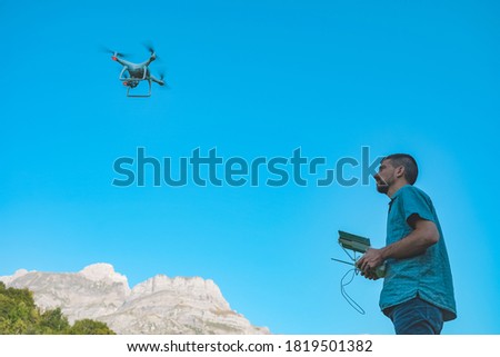 Young man with flying drone over  sunny green nature. Man operating a drone with remote control taking aerial photos and videos. Adventure concept. 