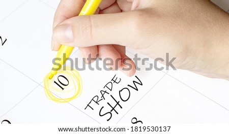 hand encircles a date on a calendar with text Trade Show yellow felt-tip pen