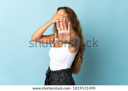 Young blonde woman isolated on blue background making stop gesture and covering face