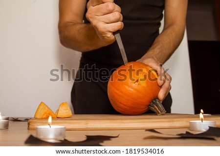 A man carves eyes and a mouth in a pumpkin for Halloween.