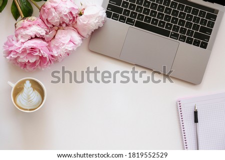 Cropped shot or laptop computer keyboard, cappuccino and the bouquet of peony flowers with a lot of copy space for text on textured table. Close up, top view.