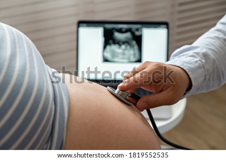 Pregnant woman at doctor's office for the regular check up. Cropped shot of unrecognizable female in the third trimester of pregnancy on physical examination. Close up, copy space, background. Royalty-Free Stock Photo #1819552535