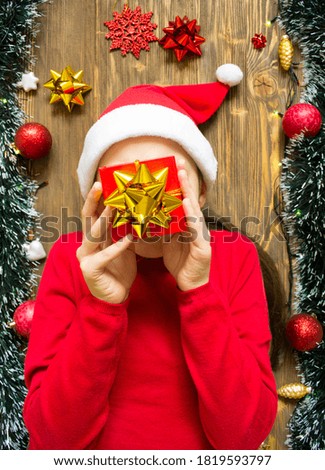 Christmas online shopping concept. Young girl wearing red sweater and Santa hat with gift box, prepare to new year, on wooden background near tinsel and lights. Winter holidays sales